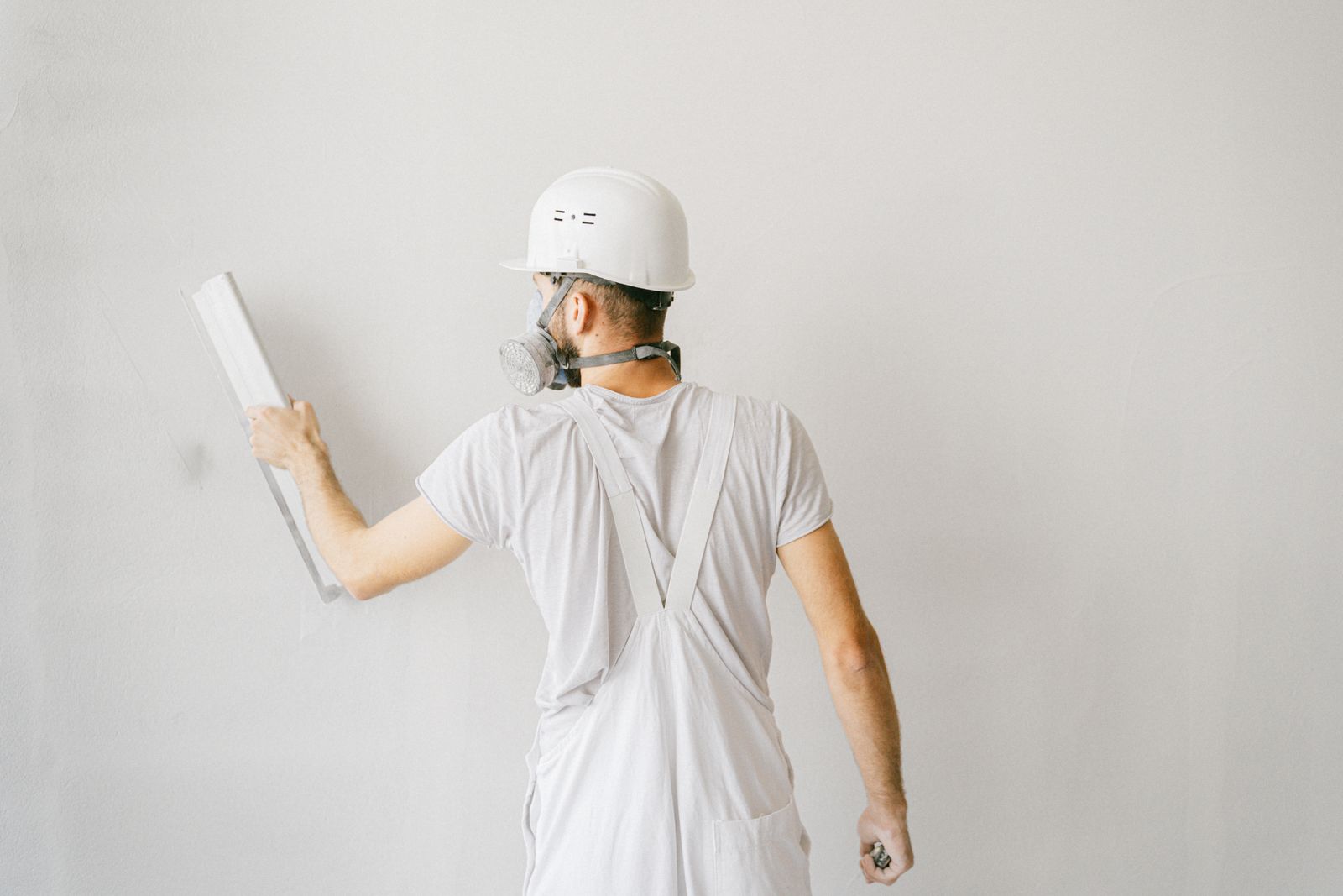 Ouvrier en tenue de protection appliquant un enduit sur le mur extérieur d'une maison